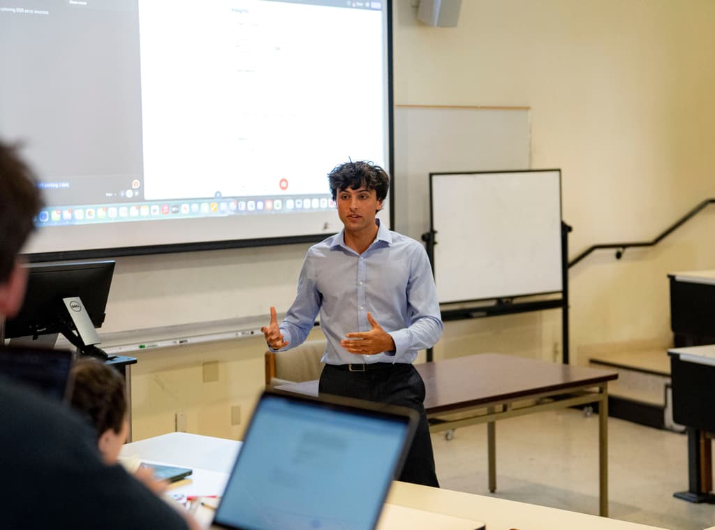 Kyle in a light blue shirt presenting to a room of students on laptops at Cal Poly Vibe Coding Club