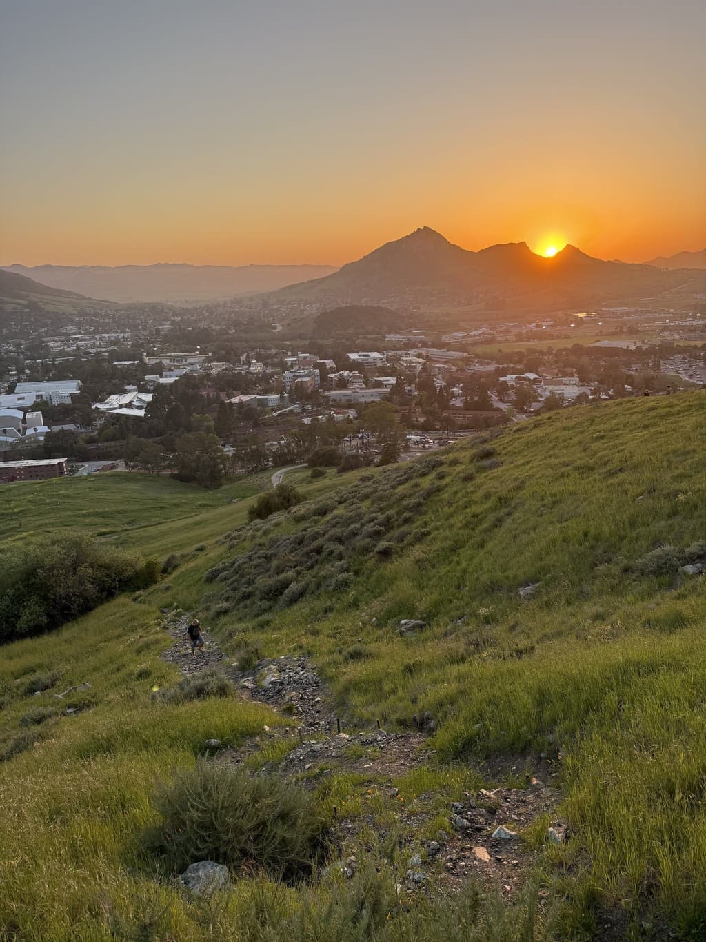 Green hills above San Luis Obispo at sunset, the town below and a peak on the horizon