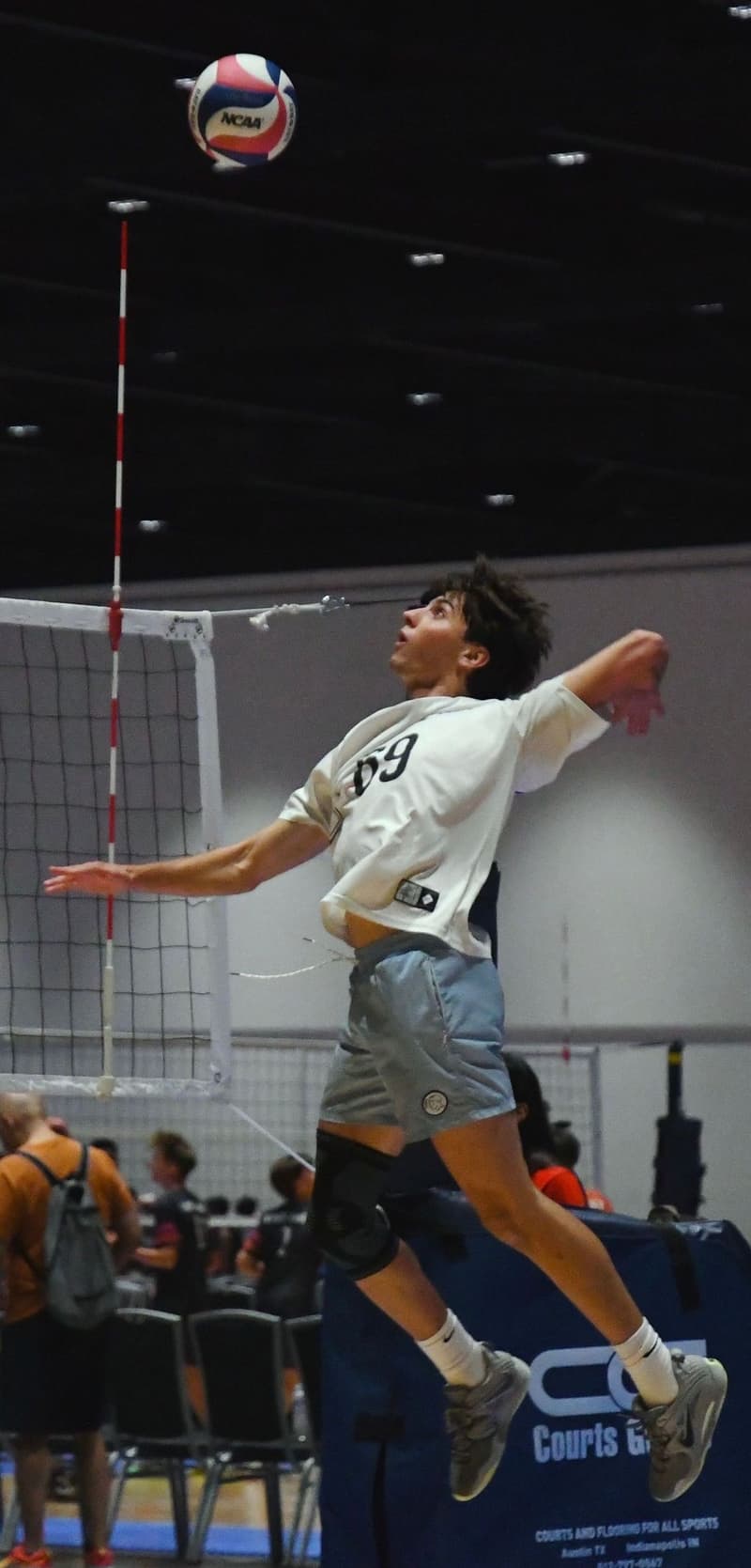 Kyle mid-air, arm cocked, about to spike a volleyball at an indoor tournament